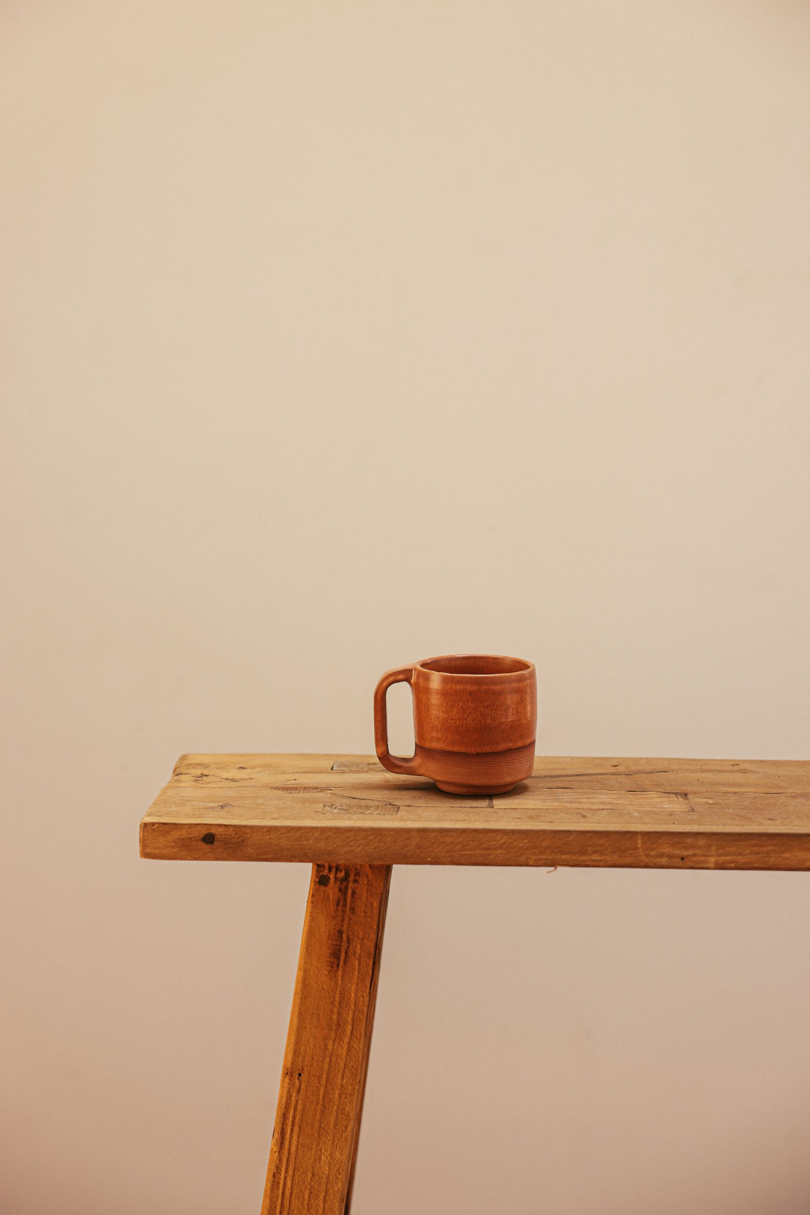 Original brown ceramic mug on a wooden bench, with a left handle and ribbed lower band